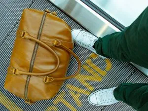 A man standing next to a brown duffel inside an airport